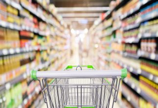 A grocery store aisle with a shopping cart in the foreground.